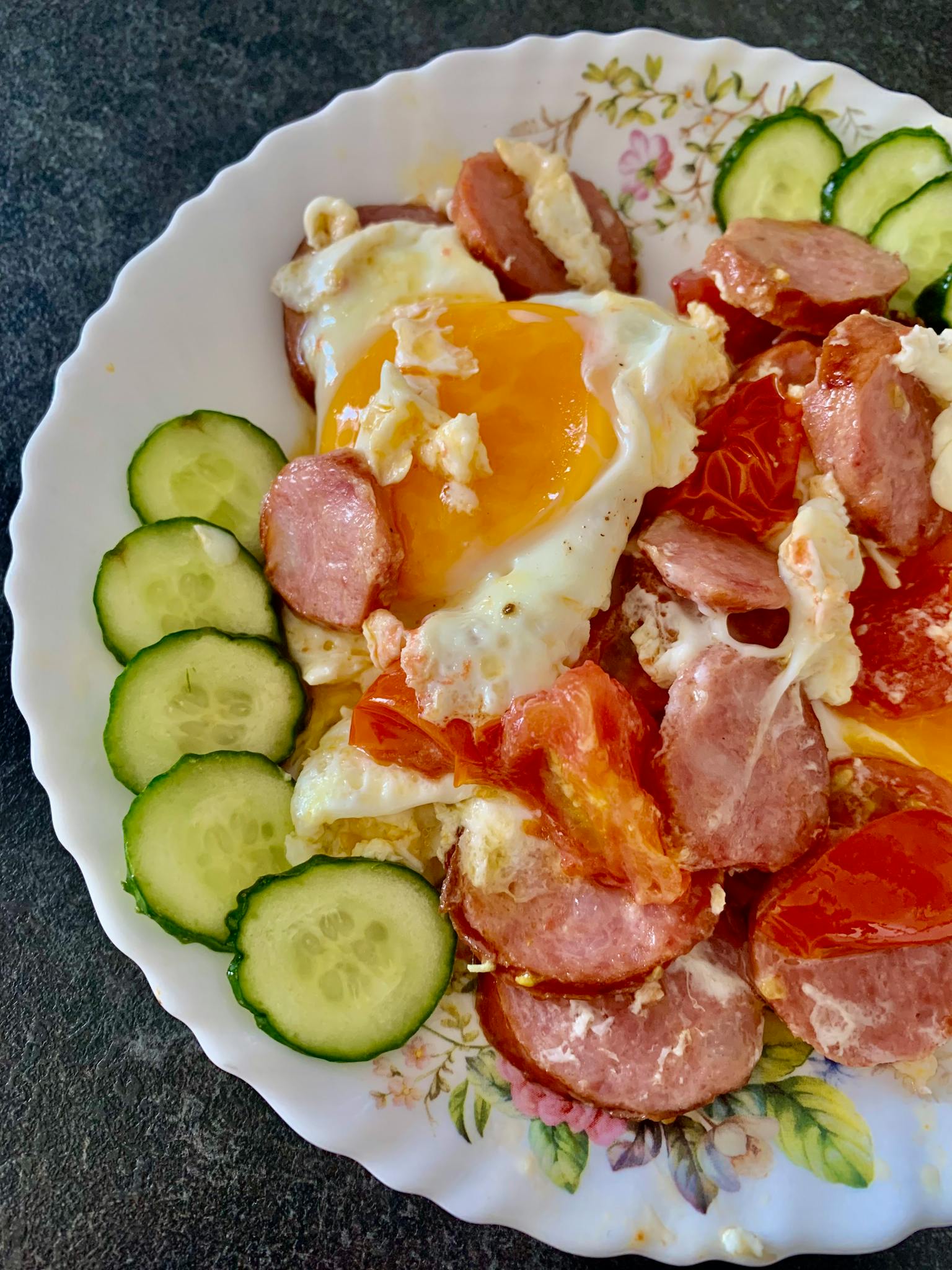 A delicious breakfast plate featuring fried eggs, sausages, and fresh cucumbers.