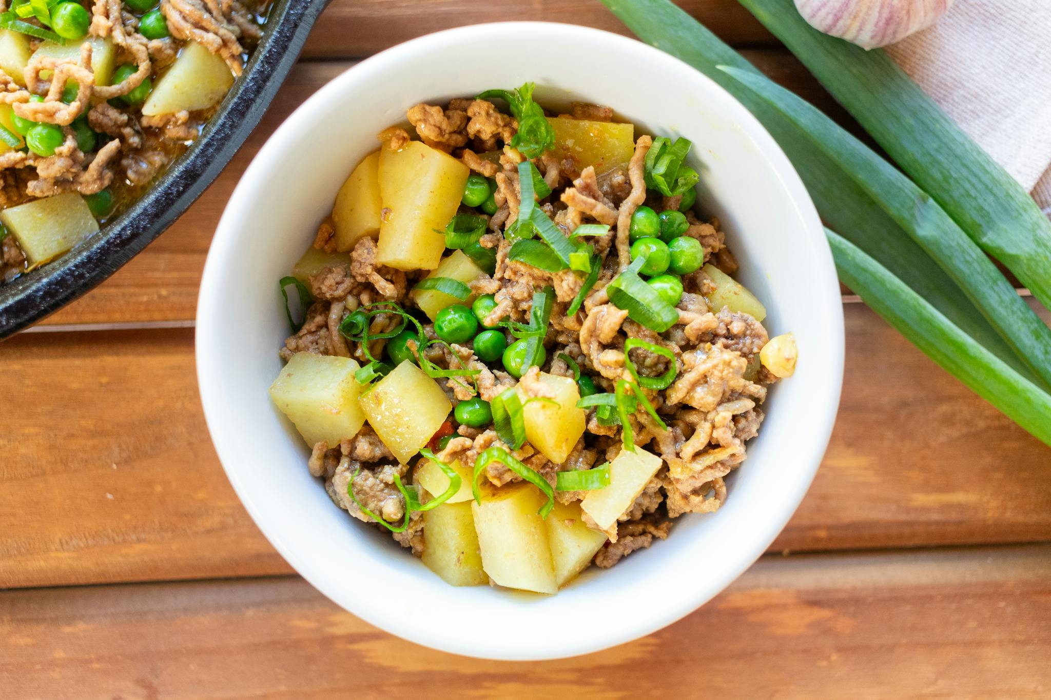Delicious minced meat stew with potatoes and green peas, garnished with fresh herbs in a white bowl.