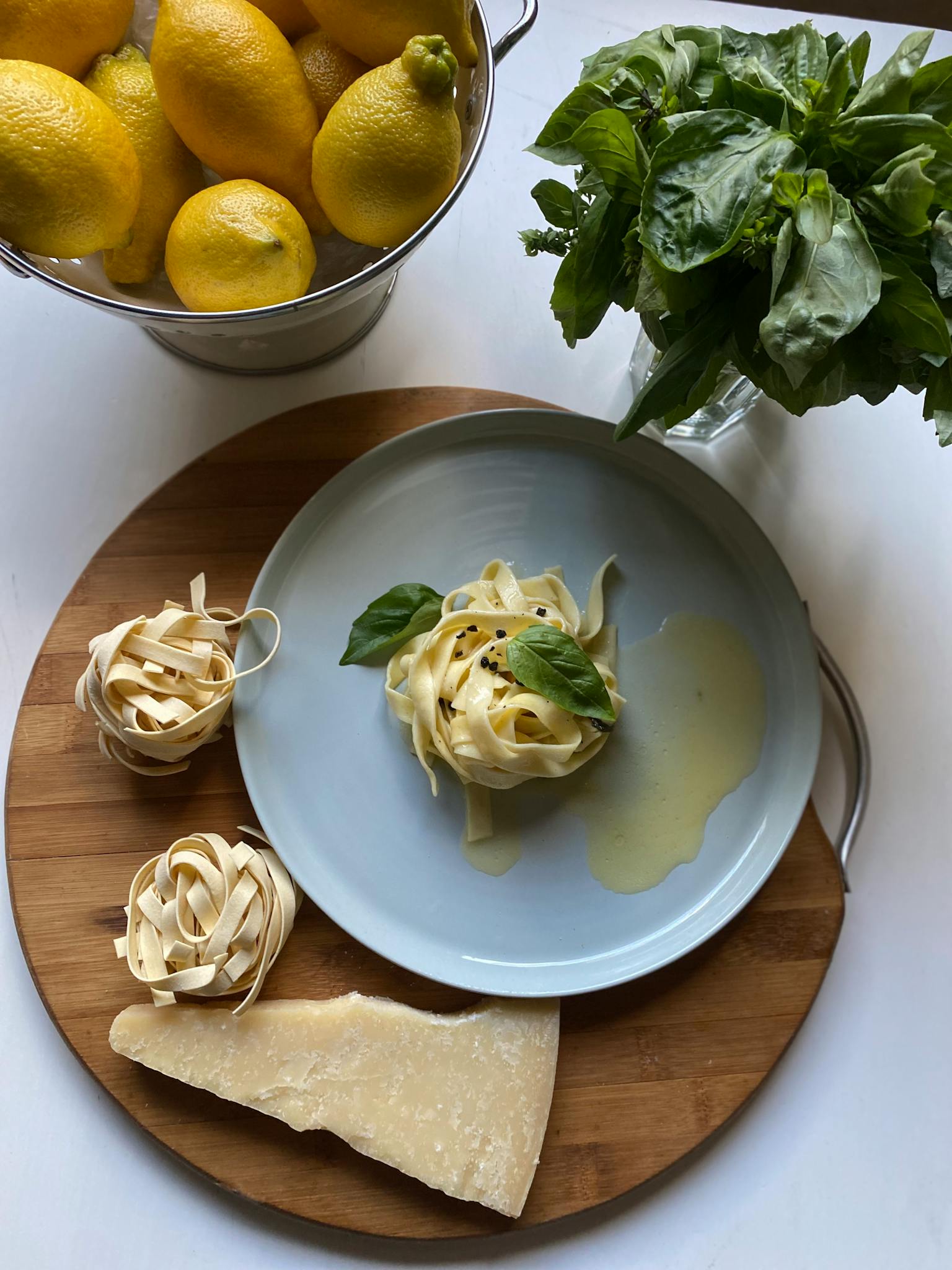 Fresh pasta with parmesan, lemons, and basil arranged on a wooden board.