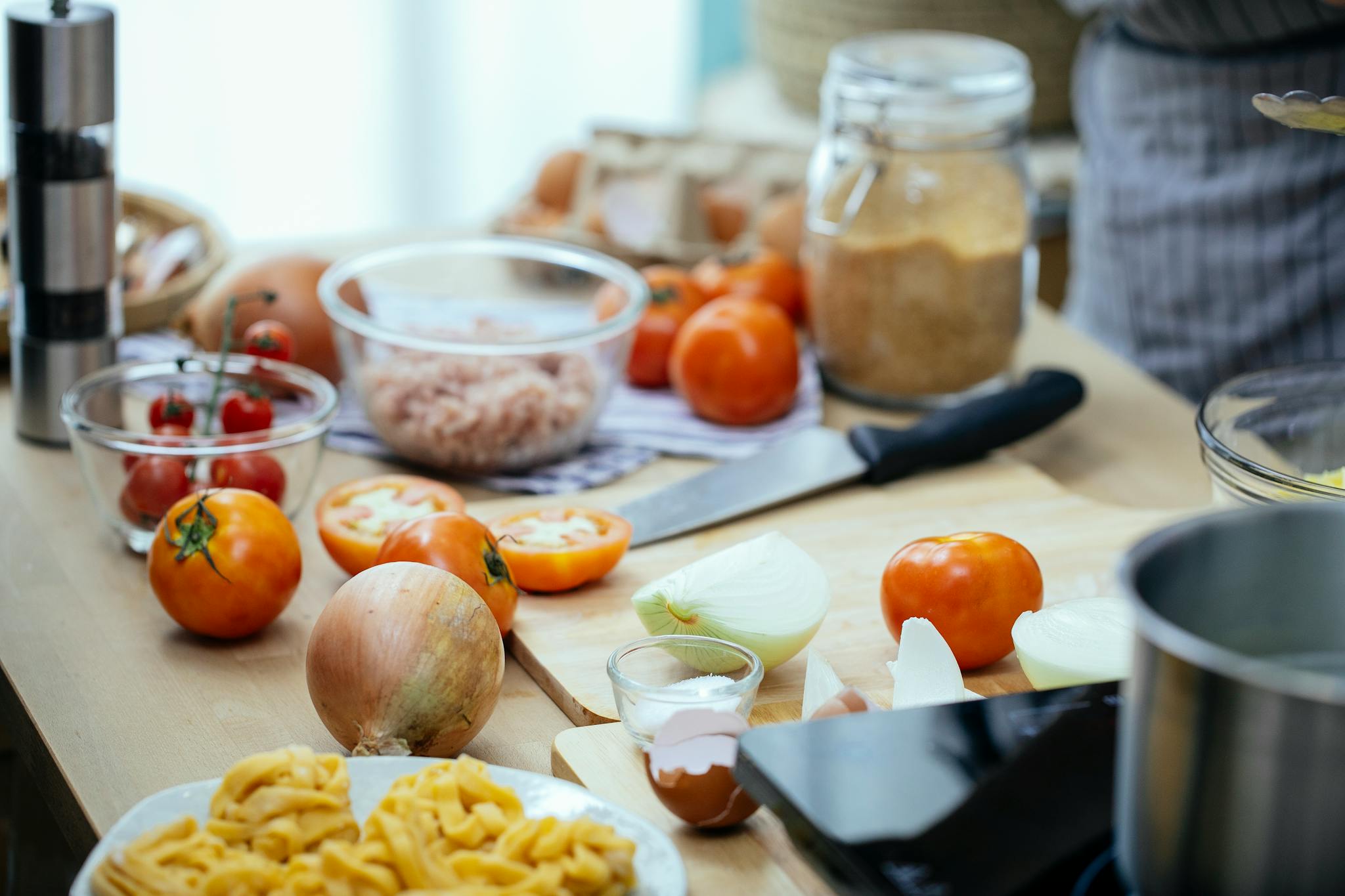 Wooden kitchen countertop with tomatoes and onions and plate of pasta during dinner preparation